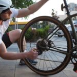 Man repairing bicycle chain and rear wheel outdoors with tools