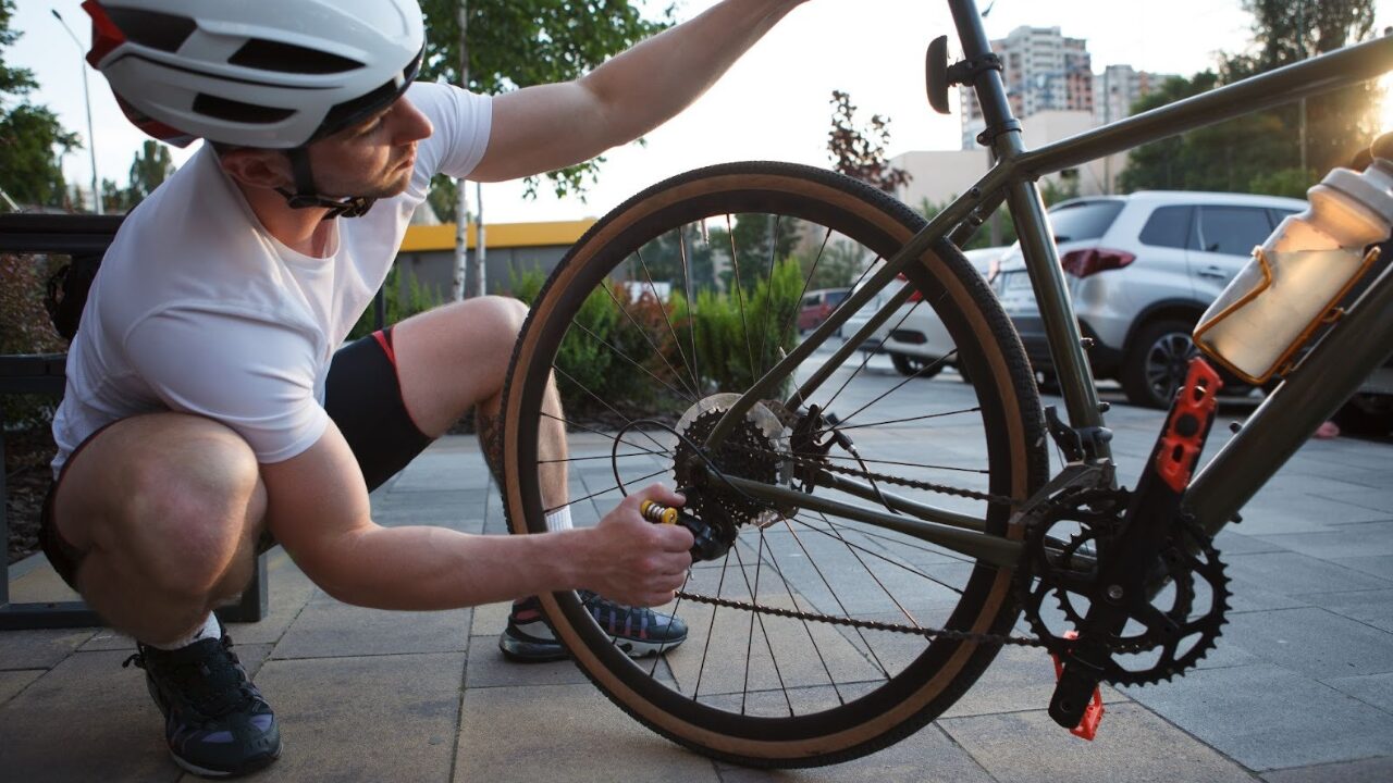 Man repairing bicycle chain and rear wheel outdoors with tools