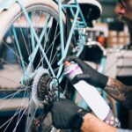 Mechanic wearing gloves applying lubricant spray to the rear gears and chain of a bicycle in a repair workshop
